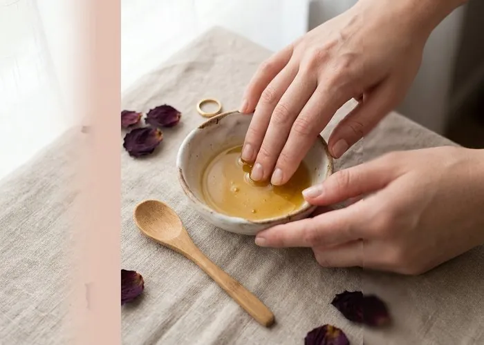 Fingertips soaking in a homemade honey and olive oil nail mask in a small ceramic bowl