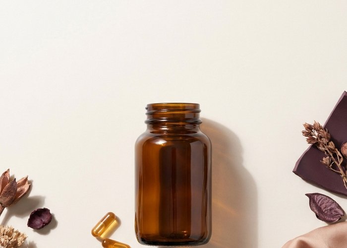 A single amber supplement bottle with two capsules resting beside it on smooth cream stone