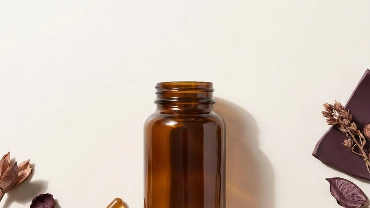 A single amber supplement bottle with two capsules resting beside it on smooth cream stone